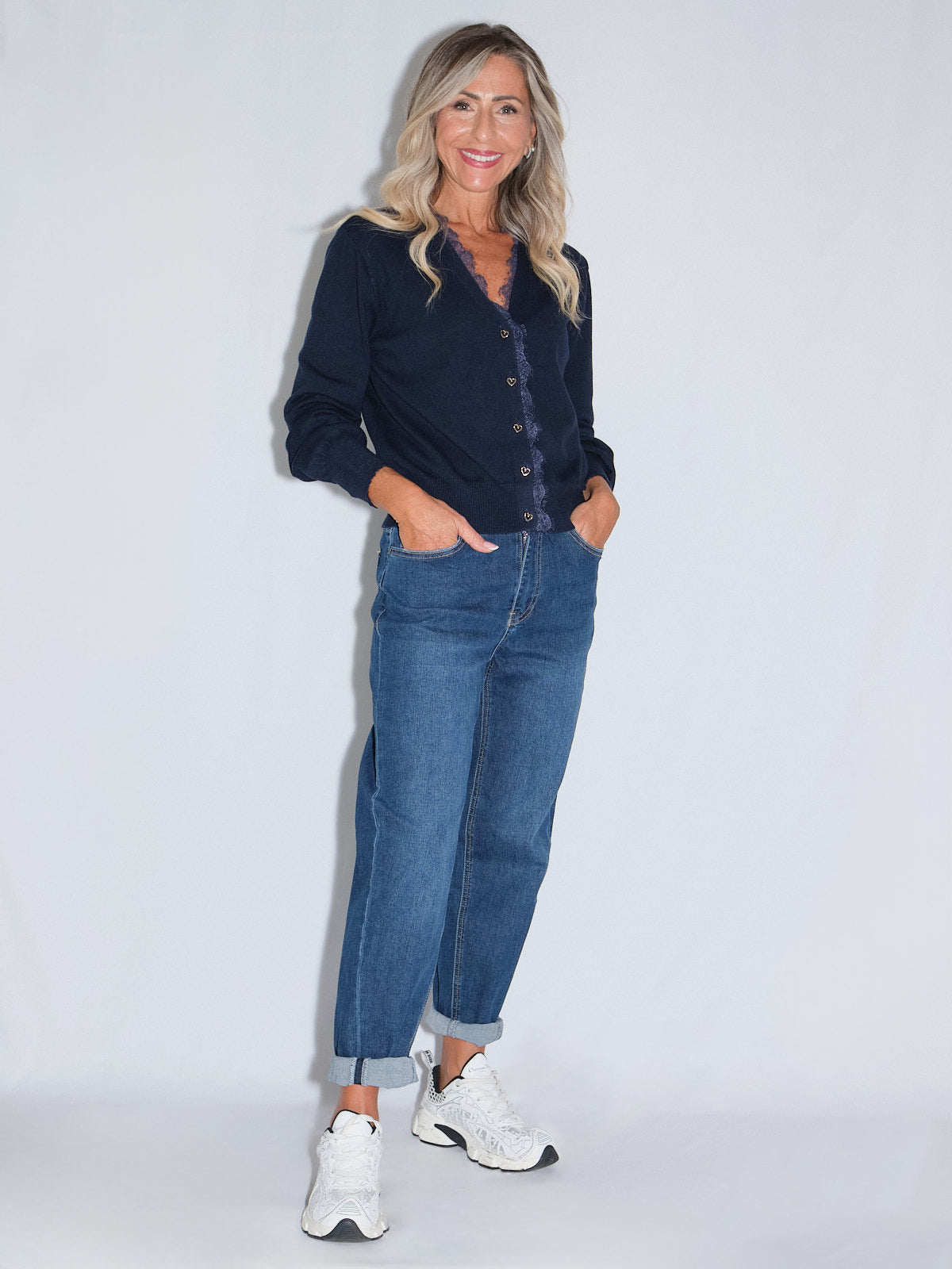 Jeans gamba dritta in blu scuro su donna con giacca nera e sneakers bianche, posa in studio.
