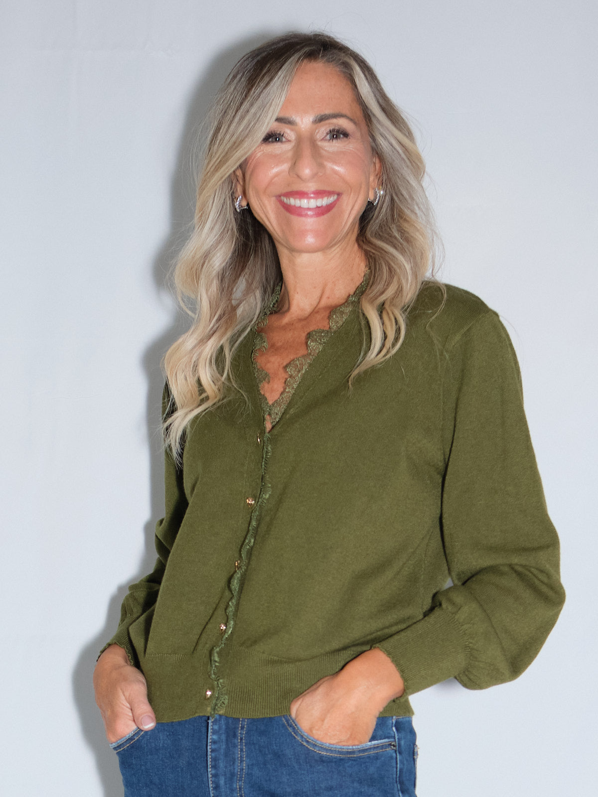 Cardigan bordato in pizzo in colore olio indossato da donna sorridente con capelli lunghi.