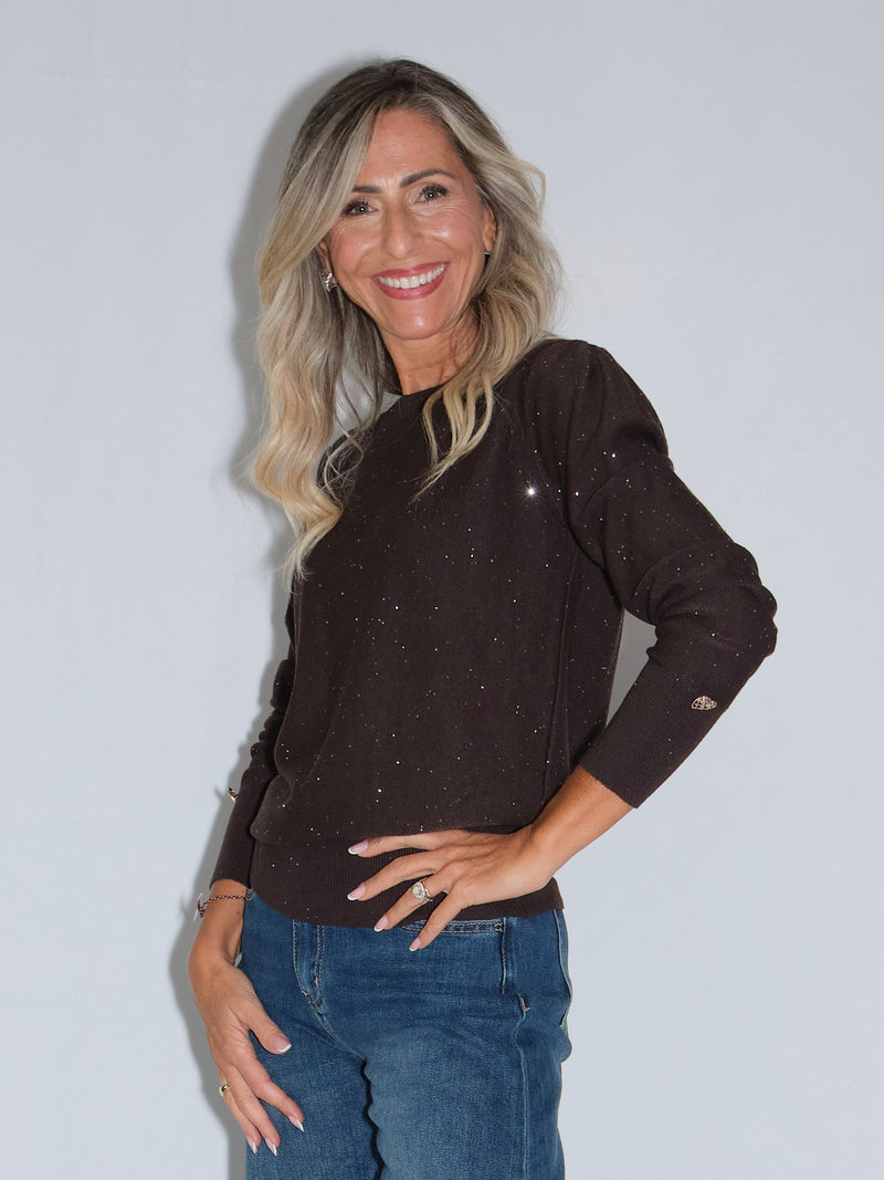 Girocollo manica lunga lurex in colore cioccolato, con dettagli luccicanti e bottoncini, indossato da una donna sorridente.