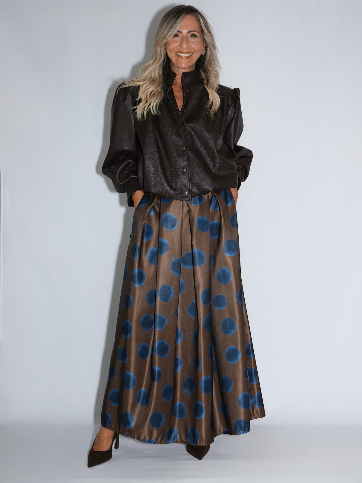 Modella in top nero e gonna a pois blu in satin, posa su sfondo chiaro per mostrare il look elegante.